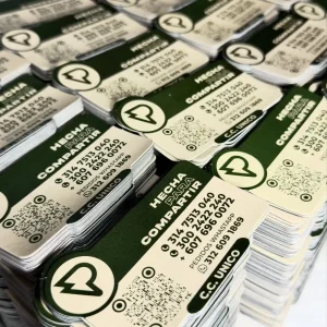 Montones de imanes publicitarios para nevera de "HECHA PARA COMPARTIR" con logo, números de teléfono, código QR y mención de C.C. UNICO.